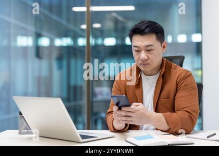 Asian man working in an office, checking his smartphone, focusing on business tasks. Stock Photo