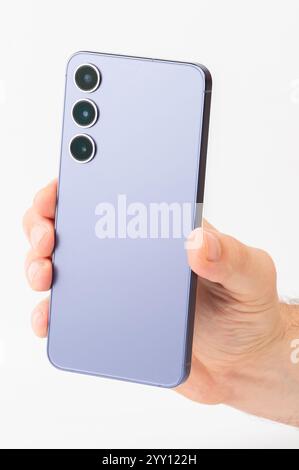 Person holds sleek smartphone featuring three distinct camera lenses in well-lit environment. Stock Photo