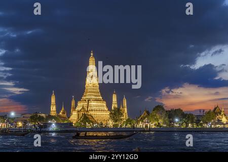 Wat Arun, Temple of Dawn at sunset with dark clouds. Boats on the Chao Phraya river. Tourist attraction in Bangkok, Thailand, Asia Stock Photo