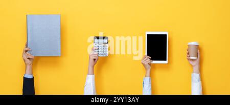 Hands raising up and holding office supplies including tablet computer, file folder, coffee cup and calculator isolated on yellow color banner backgro Stock Photo