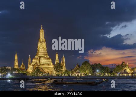 Wat Arun, Temple of Dawn at sunset with dark clouds. Boats on the Chao Phraya river. Tourist attraction in Bangkok, Thailand, Asia Stock Photo