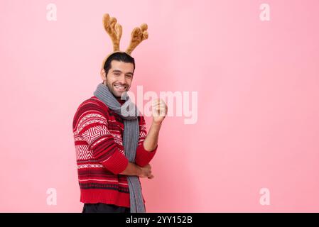 Christmas studio shot portrait of cheerful smiling handsome Caucasian man wearing red sweater and reindeer fancy headband in pink color isolated backg Stock Photo