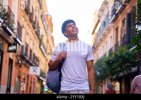 Young Latino man smiling and looking up while walking down city street Stock Photo