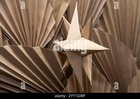 A charming paper star ornament is suspended against a backdrop of intricately folded brown paper. The unique texture and shapes create a captivating v Stock Photo