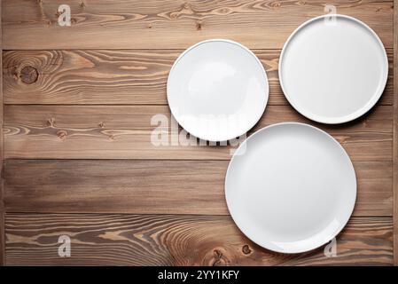 Tree empty white plates on larch wooden table, top view, copy space for your design. Food or menu template background, catering meal mock up. Stock Photo