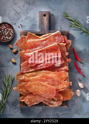 Smoked pork and chicken meat chips on wooden tray surrounded by various ingredients on table, top view of beer snack Stock Photo