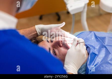 Dentist wearing gloves and a mask conducting a thorough dental checkup on a patient reclining in the dentist chair, utilizing a dental mirror along wi Stock Photo