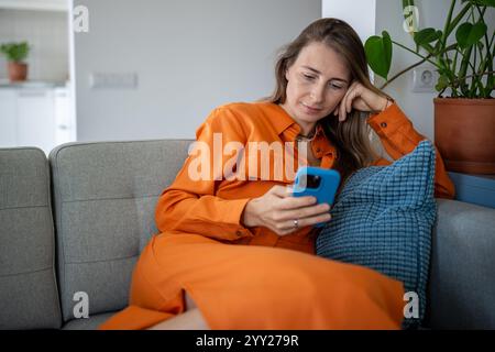 Calm focused woman use cellphone sitting on sofa making online purchases or order delivery. Stock Photo