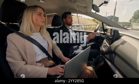 Business couple Caucasian man woman workers businessman businesswoman female male auto driving to work hurry lateness using laptop in car automobile Stock Photo