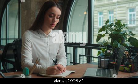 Caucasian thoughtful female university student girl studying desk office write in notebook pensive thinking businesswoman business woman writing notes Stock Photo