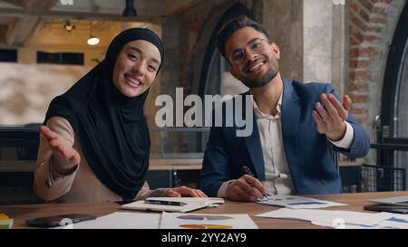 Two business partners colleagues happy male female coworkers writing at office Arabian Indian man muslim woman in hijab showing thumb up gesture good Stock Photo