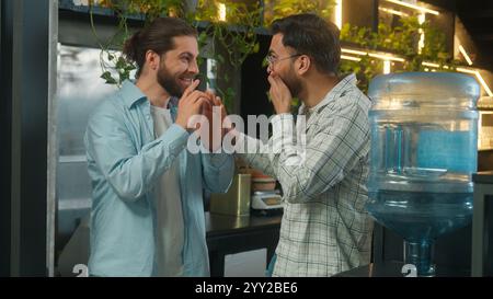 Arabian man drink water cooler in office coffee break pause two business men multiethnic businessmen colleagues coworkers Caucasian Indian guys Stock Photo