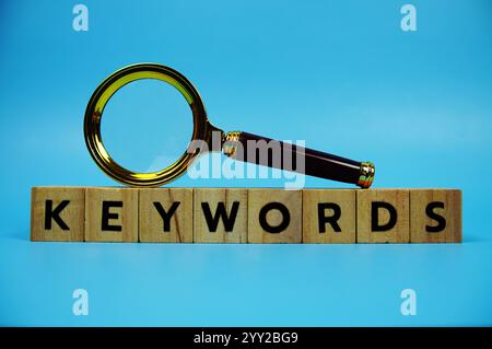 Keywords with wooden blocks alphabet letters and Magnifying glass on blue background Stock Photo