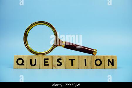 Question with wooden blocks alphabet letters and Magnifying glass on blue background Stock Photo