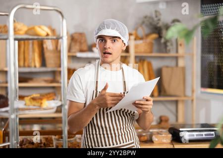 Young baker looking confused while reviewing order documents Stock Photo