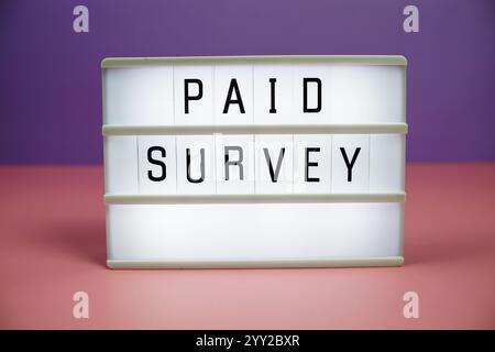 Paid Survey letterboard text on LED Lightbox on pink and purple background Stock Photo