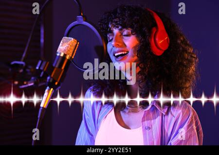 Vocalist with headphones singing into microphone in professional record studio. Sound waves Stock Photo