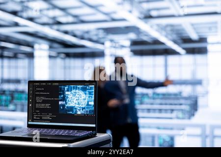 Focus on AI software on laptop in front of team of admins programming in AI data center. Close up of notebook in high tech server hub workspace used by workers upgrading artificial intelligence system Stock Photo