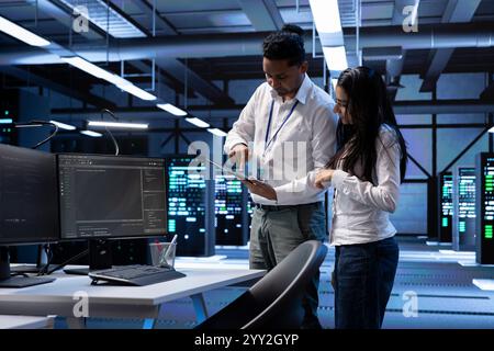 Teamworking technicians in data center looking for firewall misconfigurations affecting servers. Workers in server room check systems bottlenecks leading to sluggish data transfer rates Stock Photo