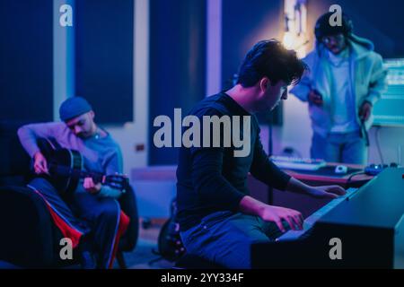 Multicultural musicians working together in a professional recording studio, playing guitar and piano, and using audio equipment. Stock Photo