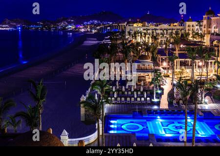 A beach with a hotel and pool at night. The pool is lit up and the hotel is lit up as well Stock Photo