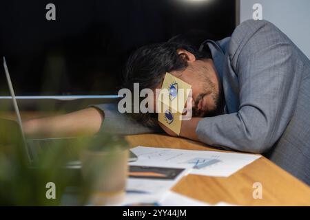 Tired sleepy businessman with stickers, adhesive notes on eyes sleeping at workplace, sitting at work desk in office, unproductive lazy employee execu Stock Photo