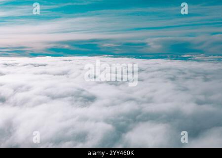 Vast expanse of clouds viewed from above from an airplane. Above the clouds, the sky is visible with a gradient of blue and gray tones, indicating var Stock Photo