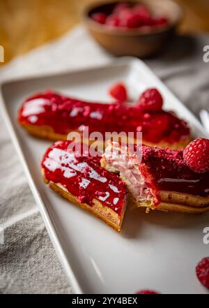Raspberry eclairs with red raspberry icing resting on white rectangular plate Stock Photo