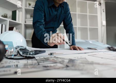 Engineer Analyzing Architectural Blueprints in Modern Office Setting with Tools and Safety Gear Stock Photo