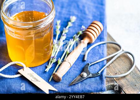 A rustic scene featuring a jar of honey with a honey dipper on a blue cloth Sprigs of lavender and scissors complete the charming arrangement, highlig Stock Photo
