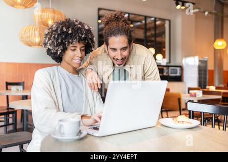 Two workers in a cozy setting are engaging with a laptop They are discussing ideas, showcasing teamwork and creativity, with warm lighting and a frien Stock Photo