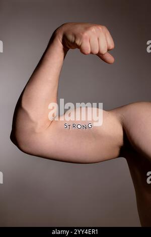 Close-up image of a flexed bicep with the word strong written on it, symbolizing power and fitness The arm is under studio lighting, emphasizing muscl Stock Photo