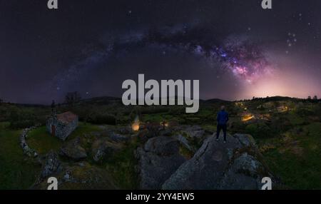A lone figure gazes at the Milky Way stretching over a serene hermitage The rural landscape and starry night create a captivating scene of solitude an Stock Photo