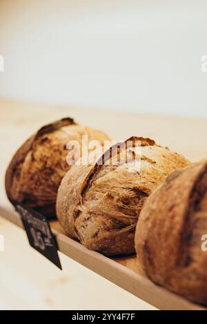 Three loaves of freshly baked artisan bread sit on a wooden rack in a cozy bakery The golden crust and rustic appearance evoke warmth and traditional Stock Photo