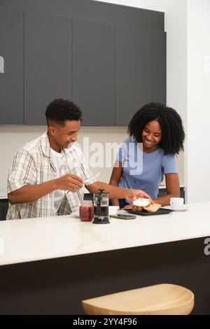 A young African American couple shares a joyful breakfast in their contemporary kitchen, smiling and enjoying each other's company over coffee and toa Stock Photo