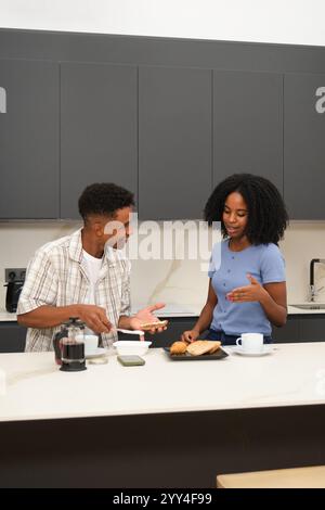 A young African American couple is seen in their modern kitchen, sharing a light-hearted conversation while preparing breakfast They enjoy coffee and Stock Photo