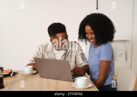 A joyful African American couple sits at a table with a laptop, sharing a laugh over coffee A cozy and intimate moment reflecting love and happiness a Stock Photo