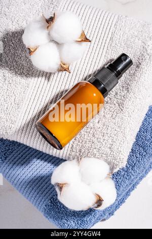 A brown spray bottle lies on folded blue and gray towels, surrounded by fluffy cotton stems. The composition evokes a sense of relaxation and natural Stock Photo