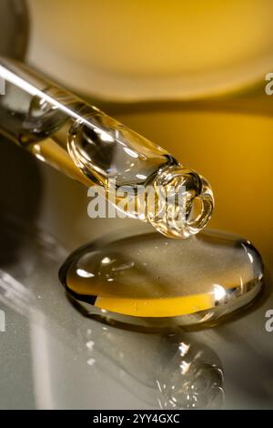 A close-up image of a glass pipette releasing golden liquid onto a reflective surface. The rich color and shiny texture provide a sense of luxury and Stock Photo