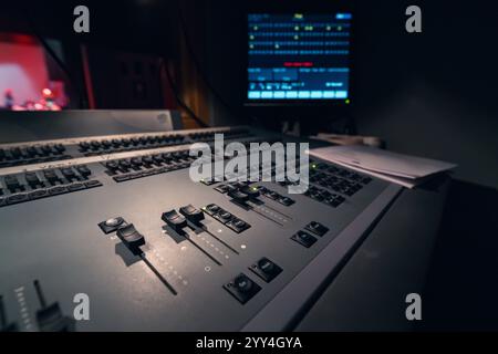 A close-up view of a professional audio mixing console in a dimly lit studio setting. The control panel features numerous buttons and sliders for prec Stock Photo