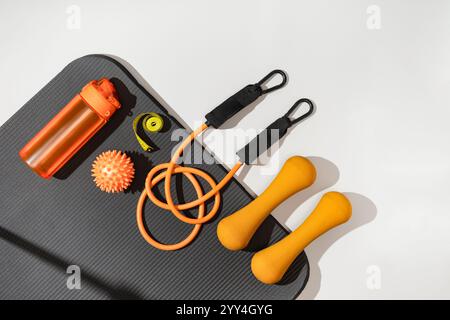 Assorted fitness equipment arranged neatly on a yoga mat showcasing dumbbells, a kettlebell, fitness bands, an expanders, massage roller, and massage Stock Photo