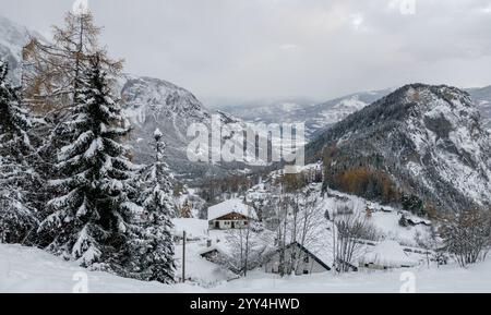 A tranquil Swiss alpine village nestled amongst snow-covered pine trees against a backdrop of majestic mountains during winter. Stock Photo