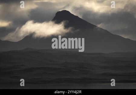 A captivating view of a rugged Icelandic mountain peak shrouded in misty clouds, creating a dramatic silhouette against the overcast sky, evoking a se Stock Photo