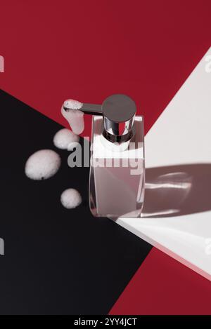 A modern liquid soap dispenser with metal accents, surrounded by bubbles on a striking black, white, and red geometric background Perfect for hygiene Stock Photo