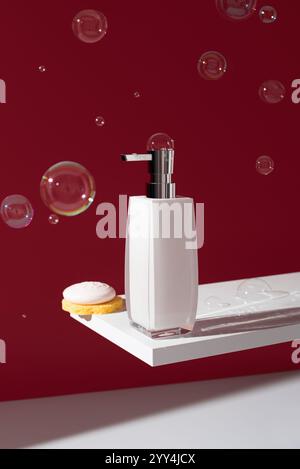 An elegant liquid soap dispenser with a bar of soap on a sponge, sits stylishly on a white shelf and a red background Decorative bubbles enhance the m Stock Photo
