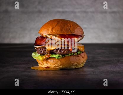 Mouthwatering burger layered with crispy bacon, fried egg, and melted cheese, served on a fresh lettuce bed with juicy beef patty, perfect for gourmet Stock Photo