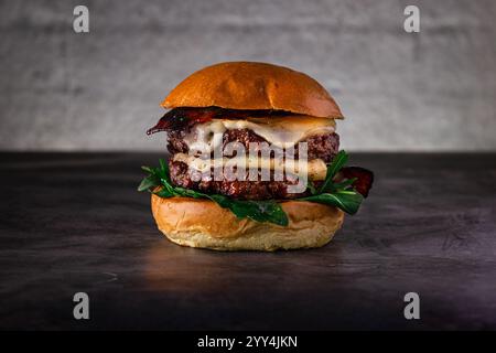 Close-up of a delicious cheeseburger with melted cheese, crispy bacon, and fresh greens, all nestled in a soft bun. The rustic table setting enhances Stock Photo