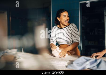 Happy female baker kneading dough on table while working in commercial kitchen Stock Photo