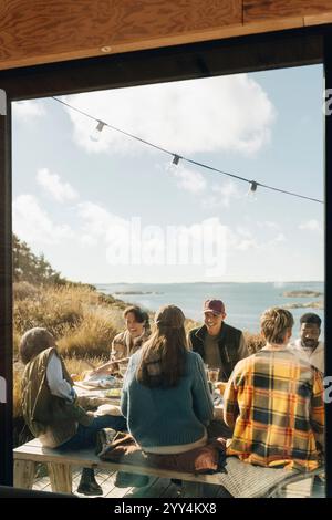 Multiracial male and female friends having dinner party on porch seen through house window Stock Photo
