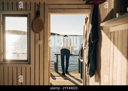 Rear view of man leaning on railing at porch of boathouse Stock Photo